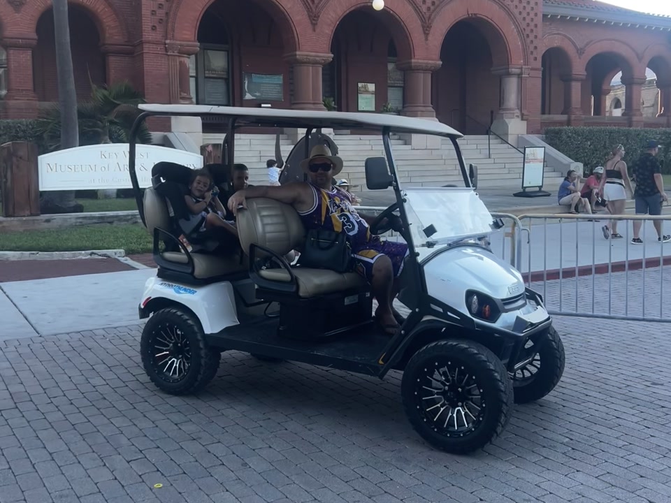 La familia de Yane en un carrito de golf blanco frente al edificio de ladrillo rojo cerca de Mallory Square
