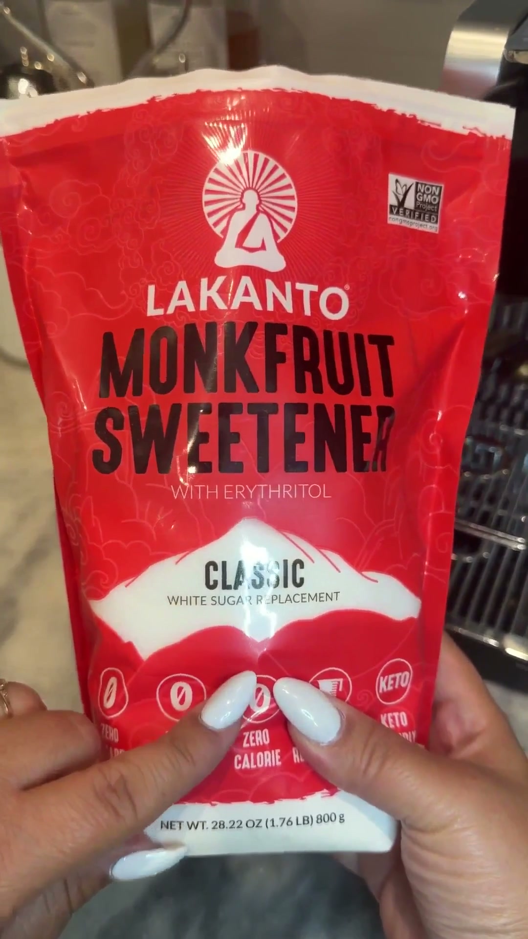 Bolsa roja de Lakanto Classic con eritritol, sostenida frente a la cafetera