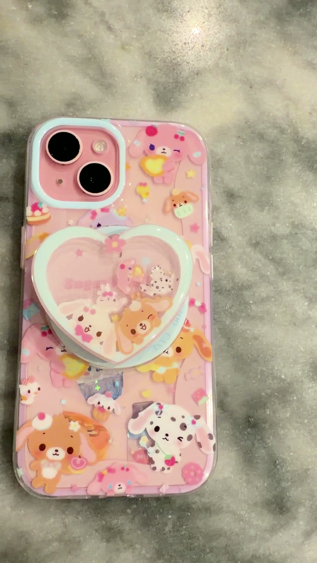 Funda rosa de iPhone con conejitos, dulces y un agarre transparente en forma de corazón