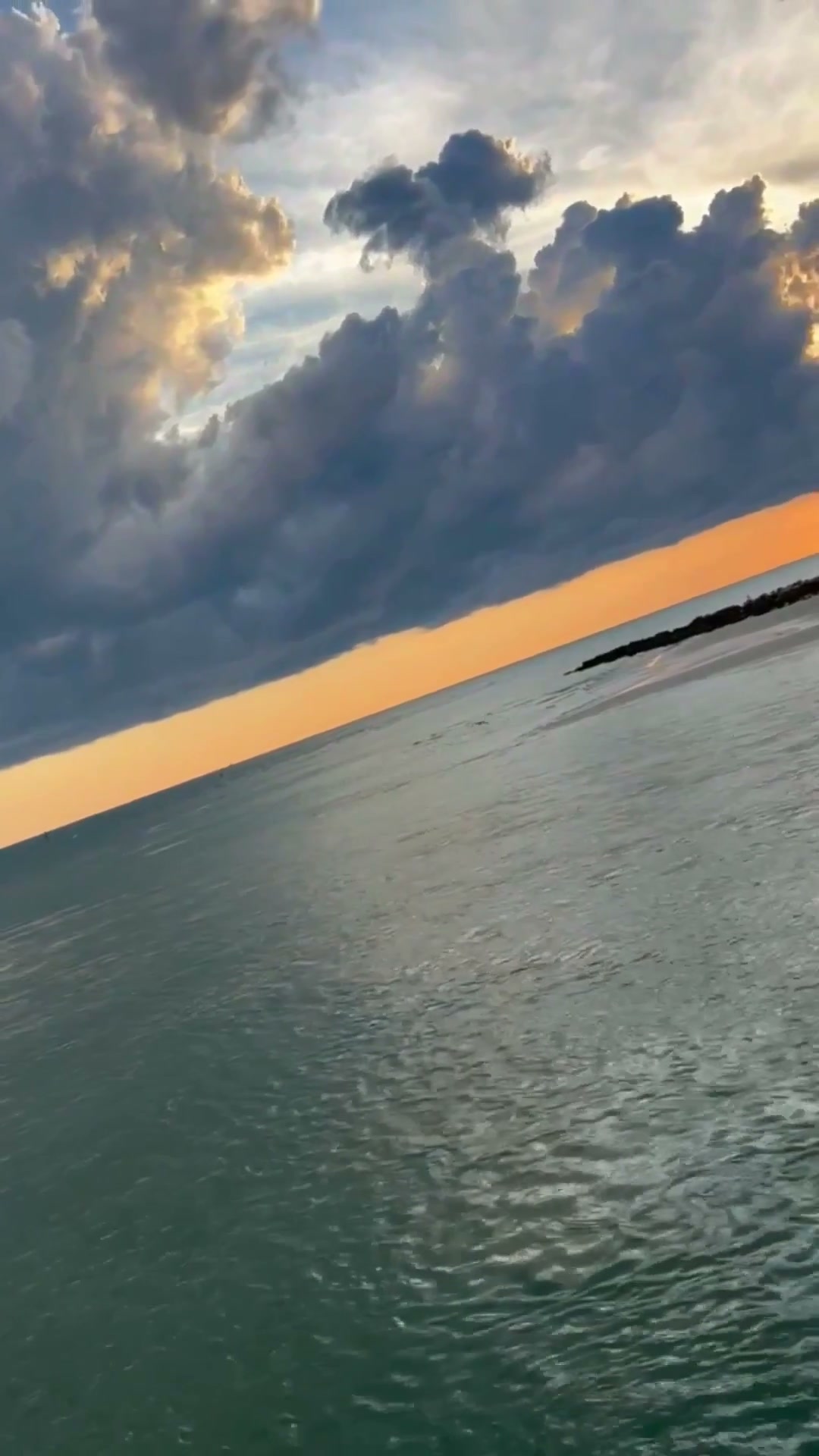Cielo naranja bajo grandes nubes sobre el agua al atardecer en Naples