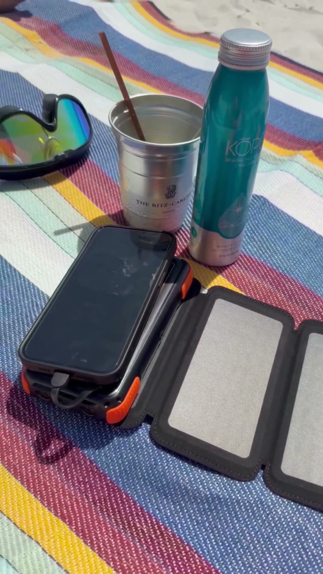 Cargador solar desplegado sobre una toalla de playa con el teléfono conectado