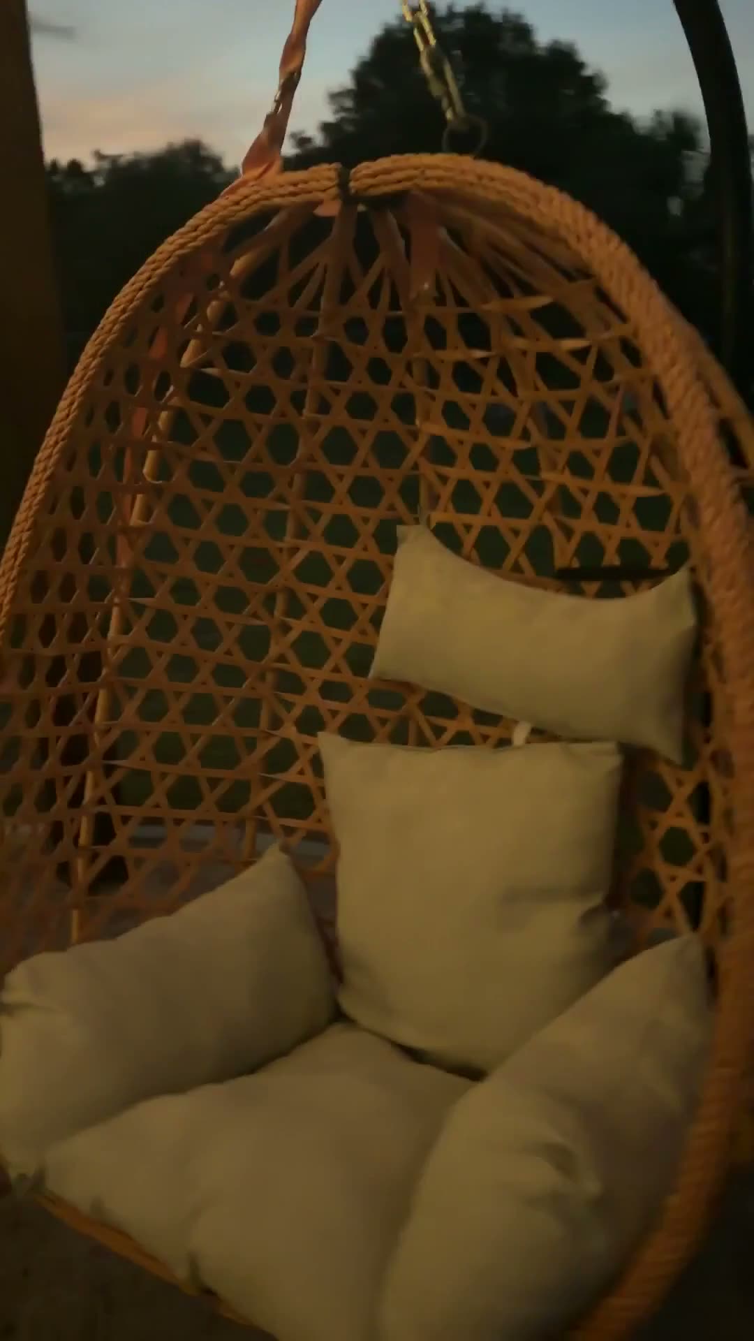 Silla colgante de mimbre con sus cojines, en el patio al atardecer